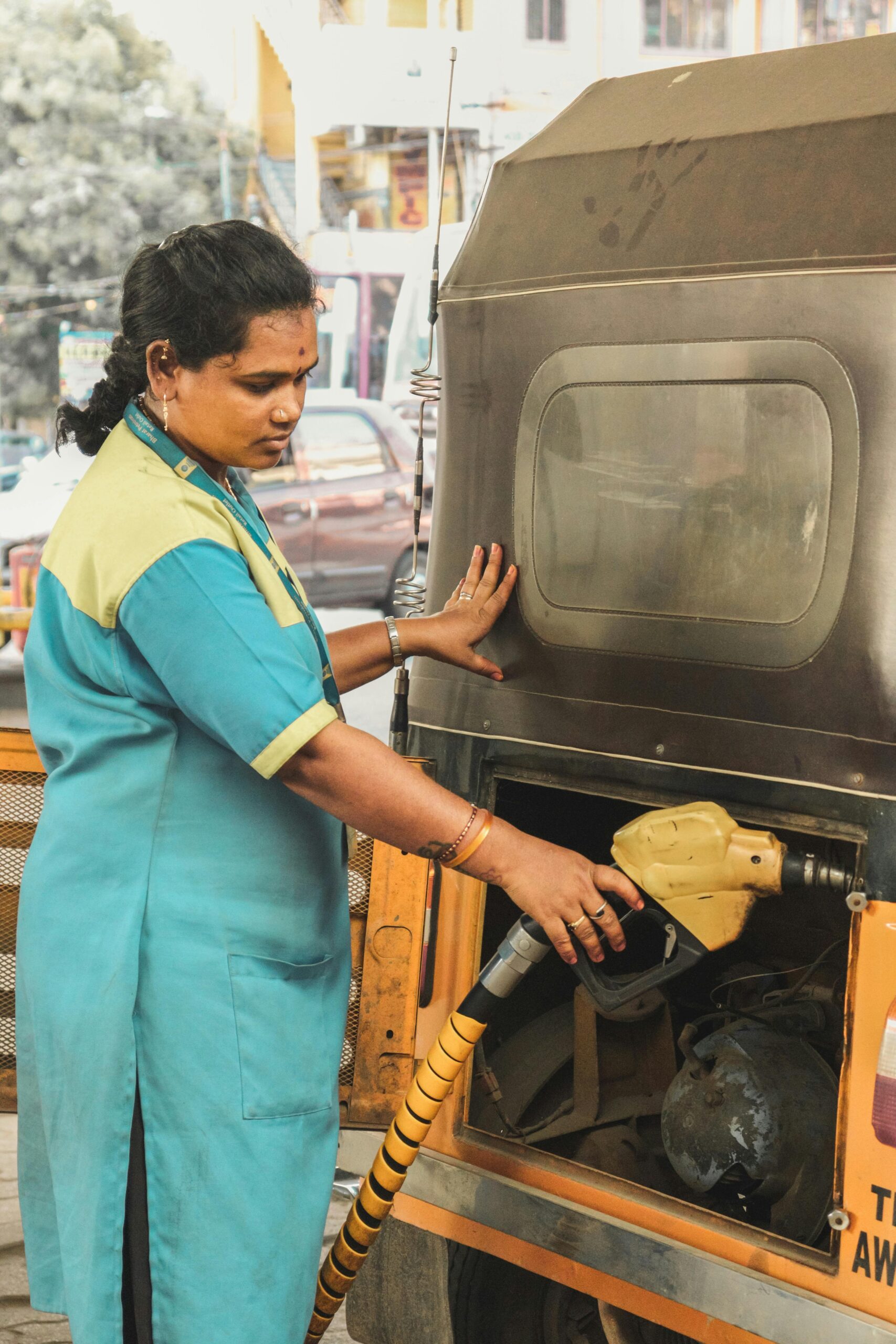 Indian woman refilling vehicle at urban gas station, demonstrating everyday life.